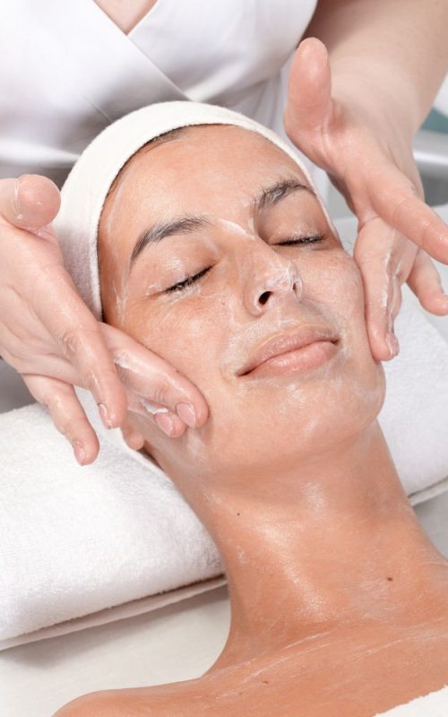 Woman Relaxing At Salon While Receiving Facial Treatment